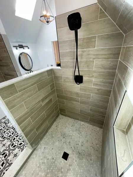 Tiled walk-in shower with gray wood-look tiles, small gray floor tiles, black shower head, and an adjacent bathroom.