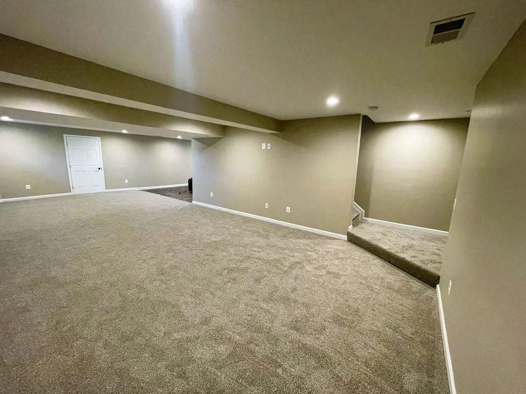 Empty basement room with neutral walls, carpet, and a set of stairs.