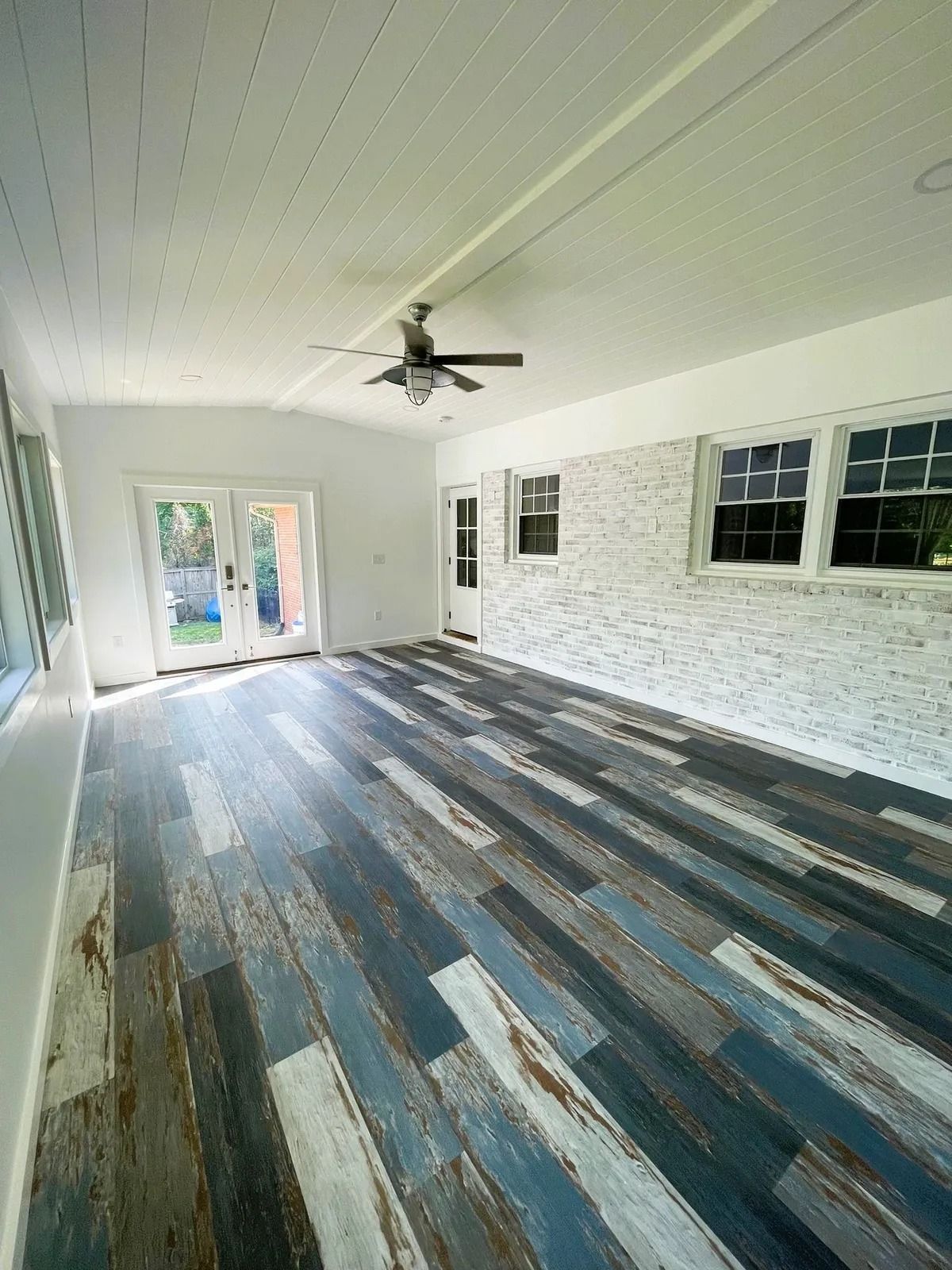 Interior view of a room with distressed blue and gray flooring, white walls, and a wood-paneled ceiling.