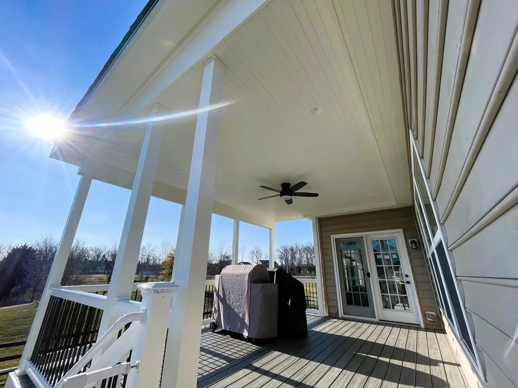 Covered porch with white pillars and railing; grill covered, ceiling fan, sunny.