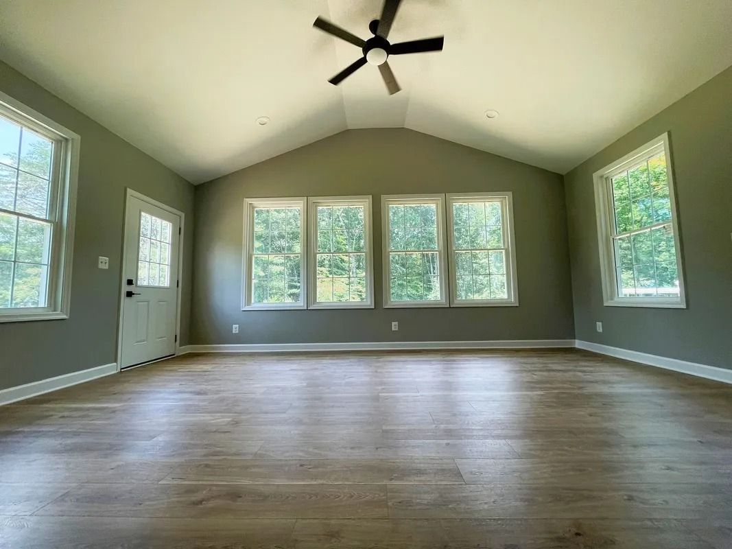 Empty room with vaulted ceiling, windows, and wood-look flooring. Walls are light green. A ceiling fan is installed.