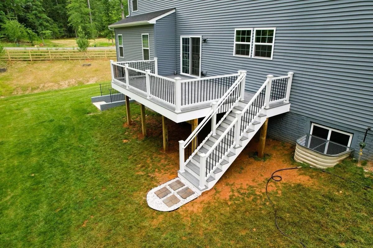 Gray house with white deck and stairs leading to a grassy yard.