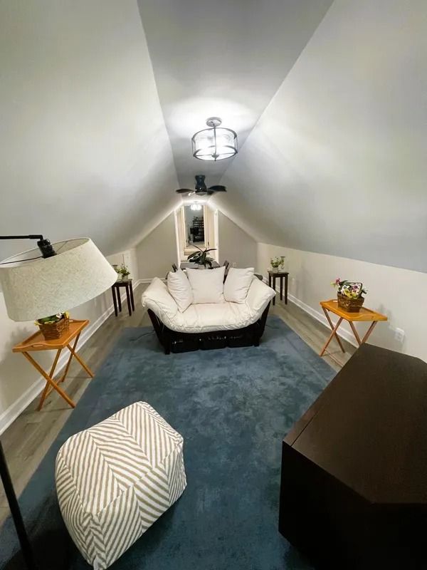 Cozy attic living room with blue rug, white sofa, side tables, and a ceiling fan.