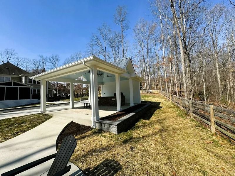 Pavilion with white columns, concrete walkway, grassy area, and wooden fence.