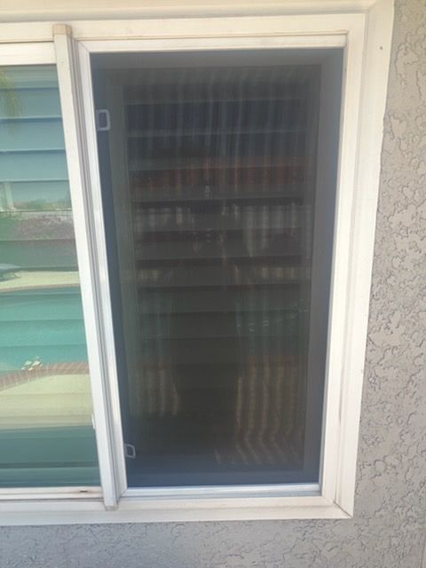 A rectangular window with a dark mesh screen installed in the frame, viewed from the exterior of a stucco home.