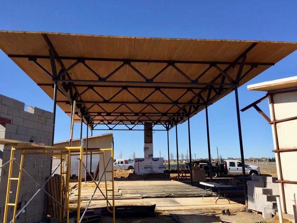 Partially built metal canopy structure at a construction site, with cinder blocks and equipment under a blue sky.