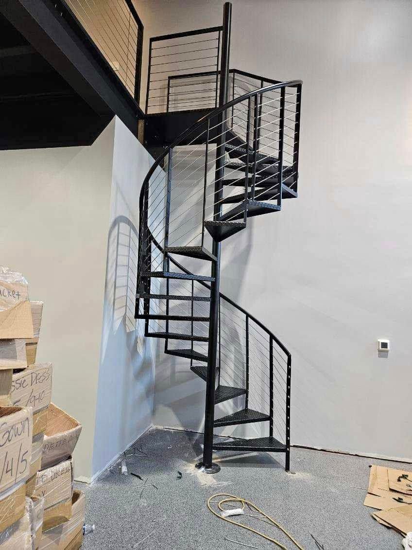 Black metal spiral staircase in a bare interior with white walls and a concrete floor.
