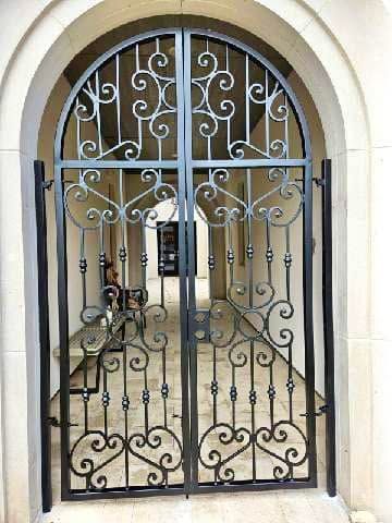 Wrought-iron gate with decorative swirls set in a stone archway entrance.