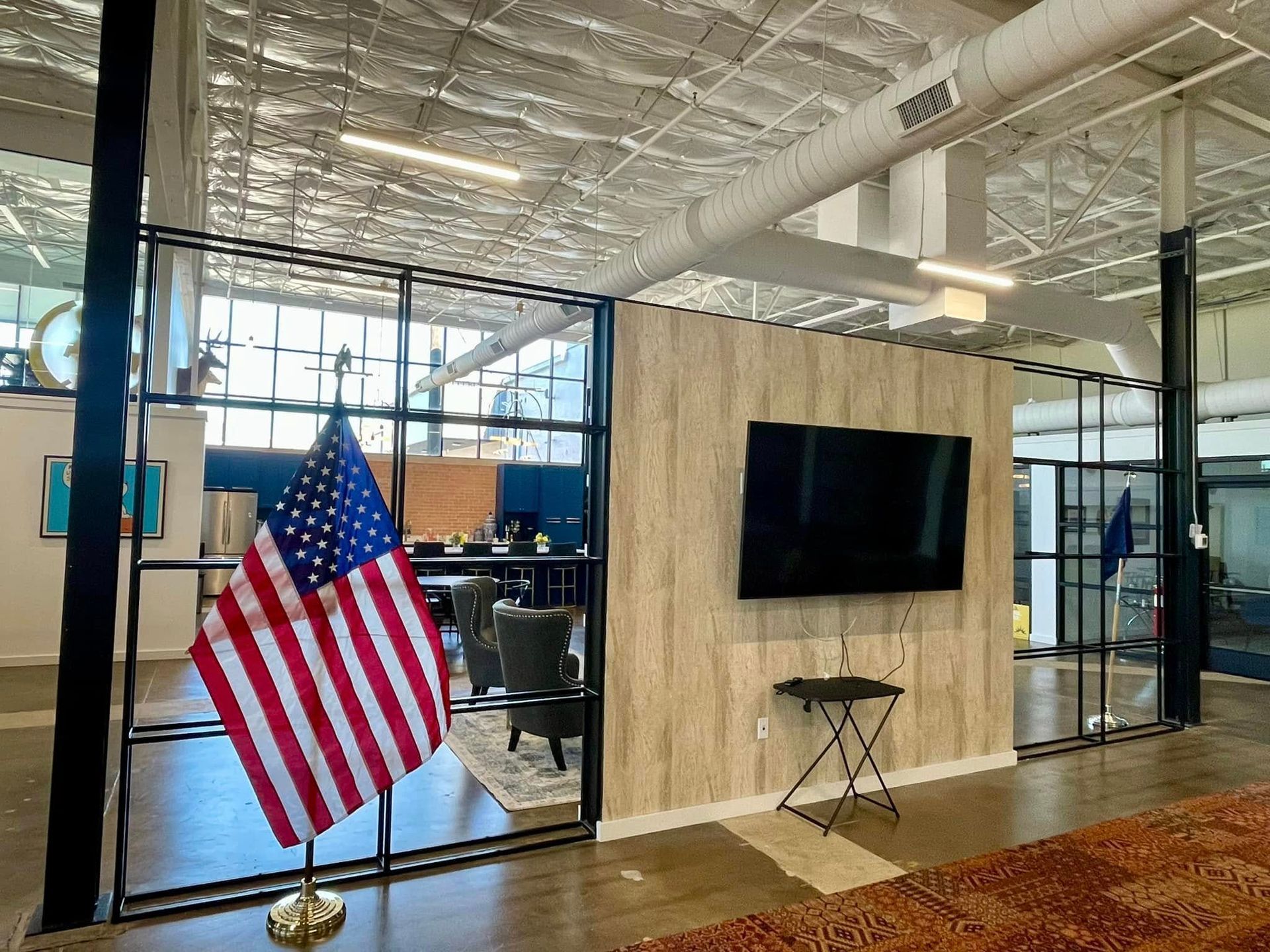 Open office lobby with a U.S. flag, wall-mounted TV, and glass-walled workspaces.