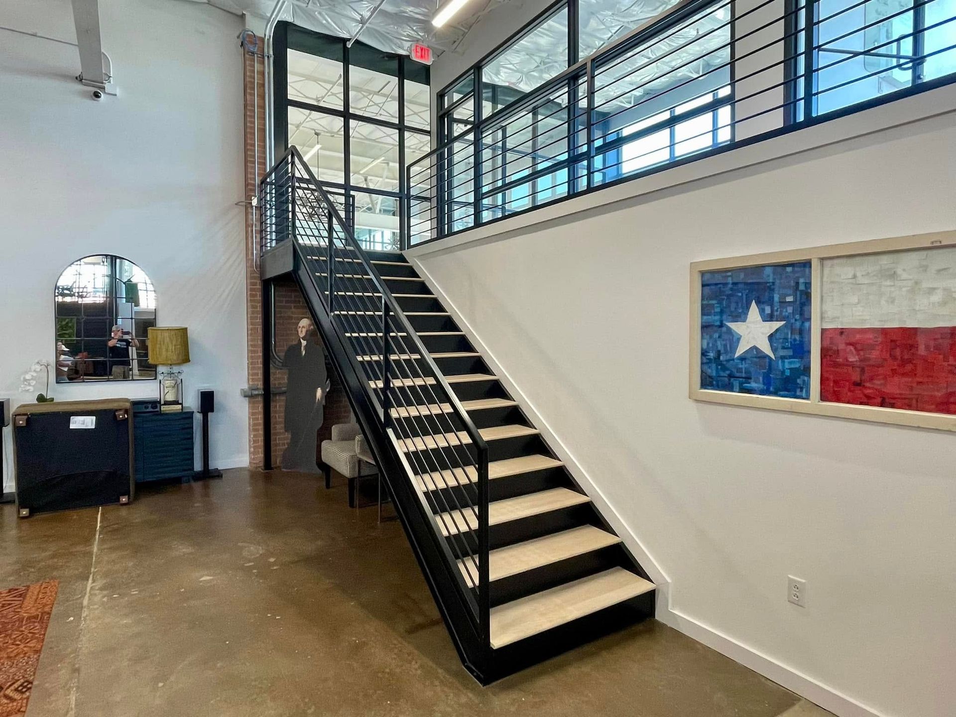 Modern lobby with black staircase, glass railings, and Texas flag wall art.