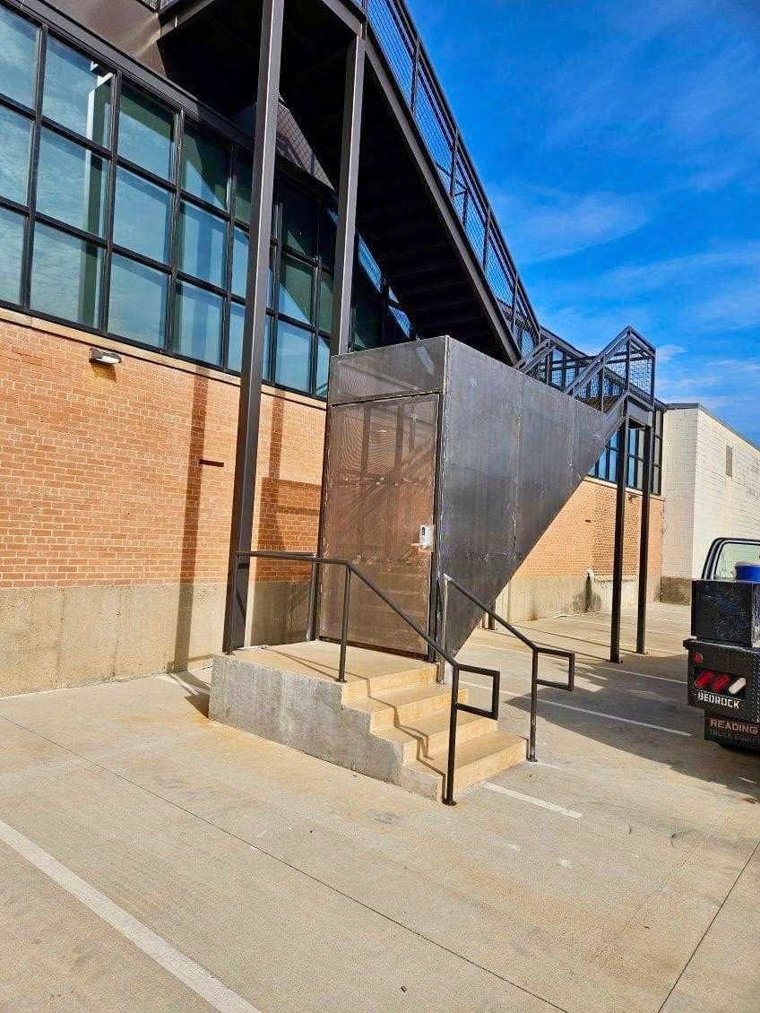 Brick building exterior with metal ramp, railings, and stair access by a concrete walkway.