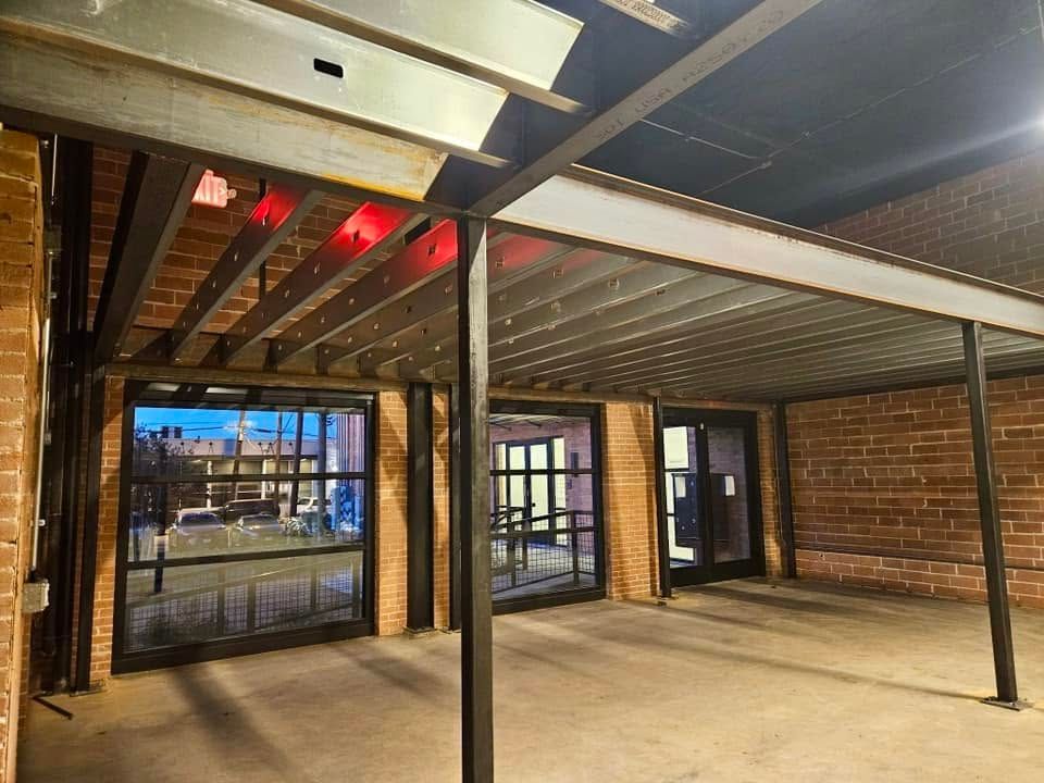 Empty indoor space with exposed beams, brick walls, black posts, and large glass doors.