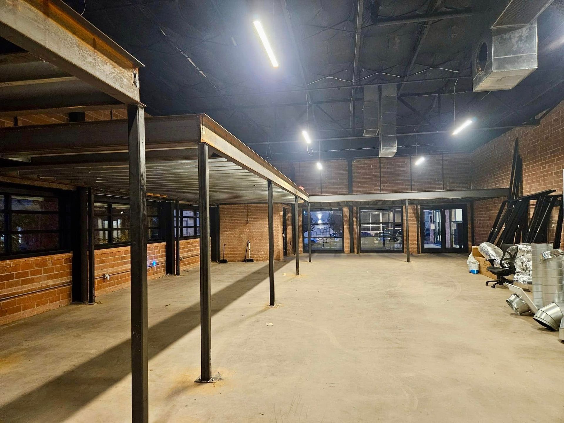 Empty industrial basement with metal shelving, exposed brick walls, and concrete floor under fluorescent lights.