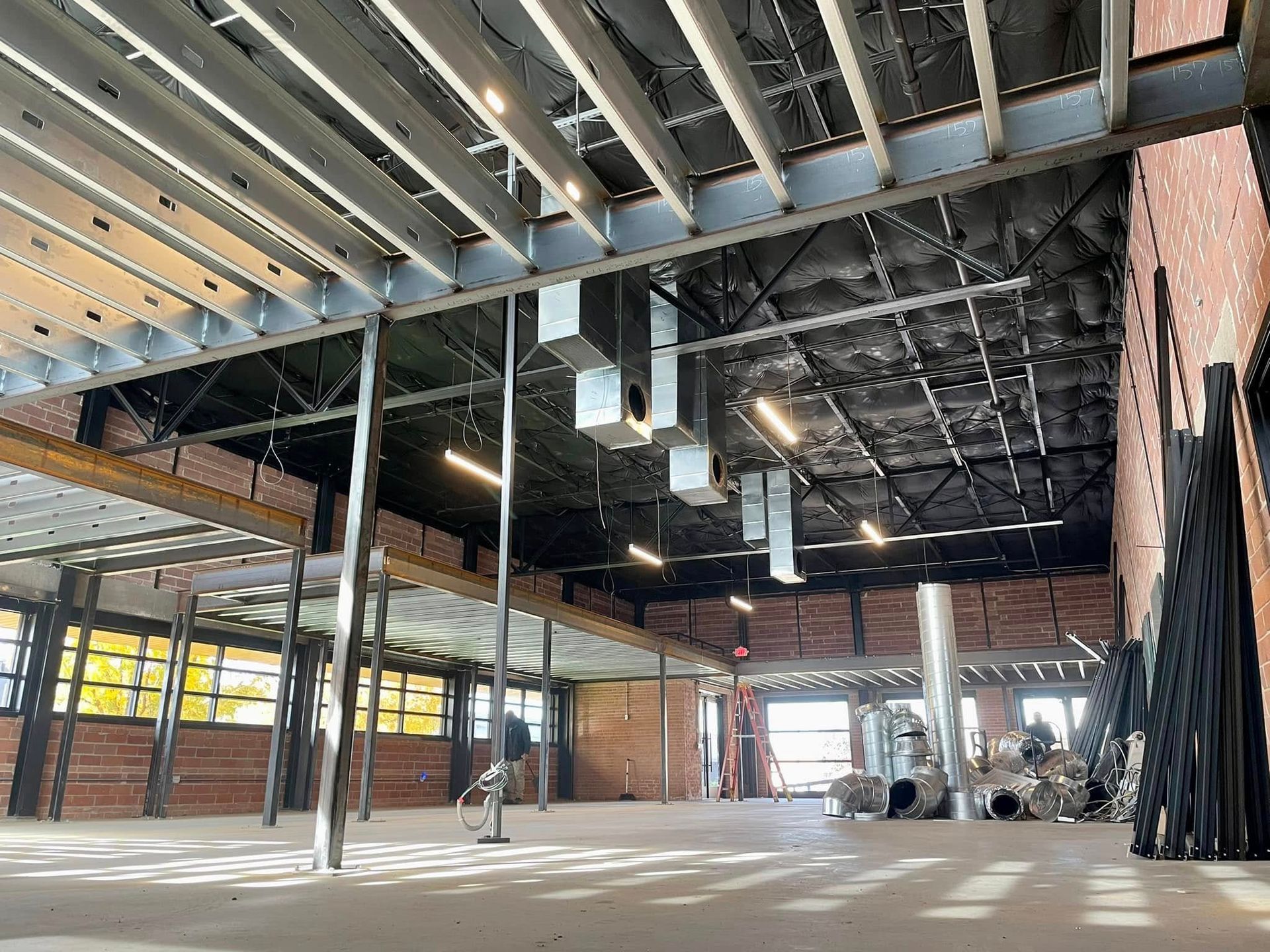 Empty, unfinished interior with exposed beams, columns, and construction materials inside a large building.