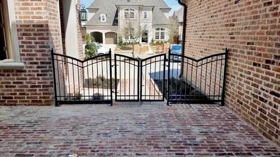 Brick patio opening to a gated walkway between brick walls, with houses visible beyond.