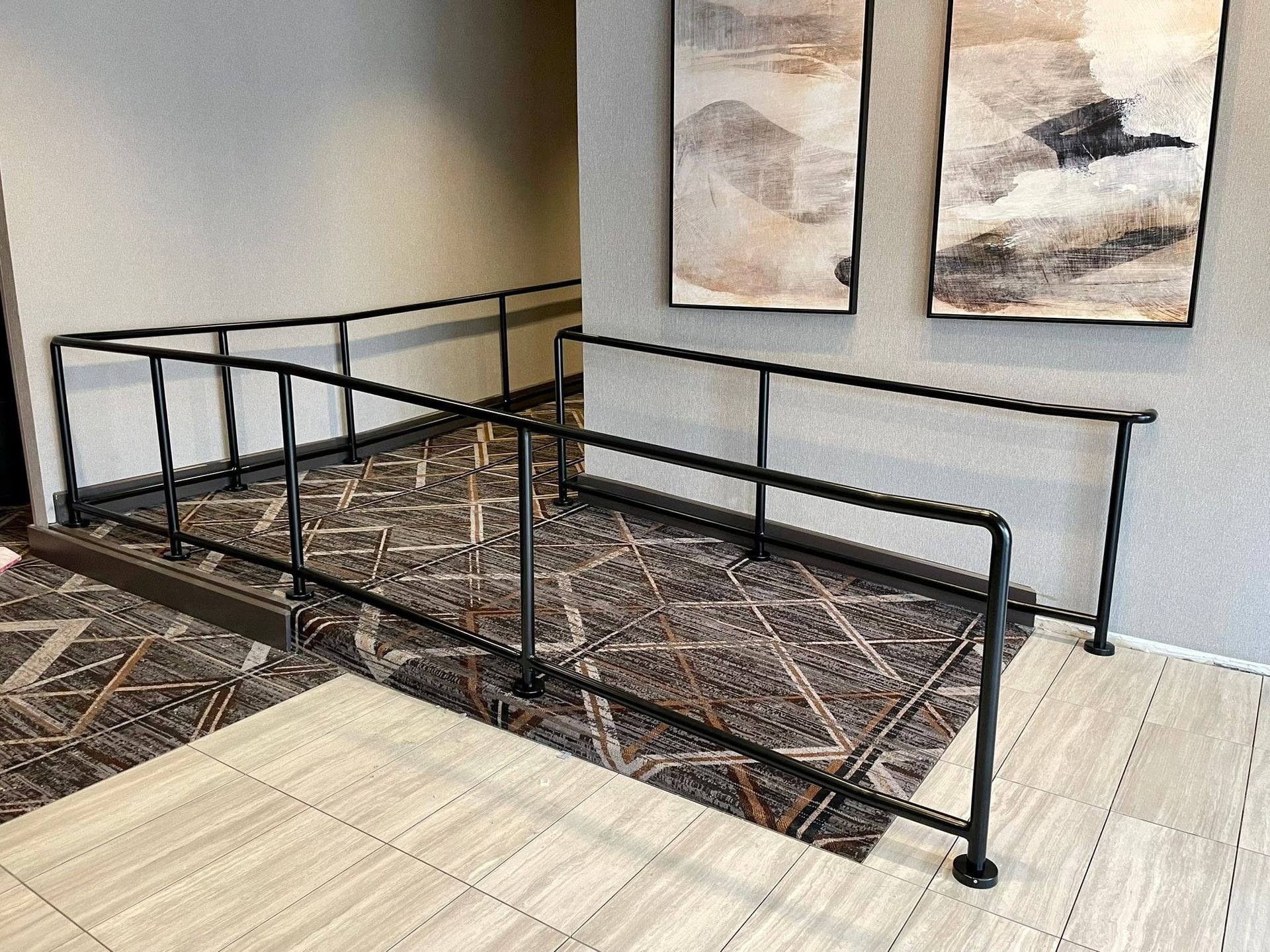 Indoor wheelchair ramp with black handrails and patterned carpet in a lobby area.