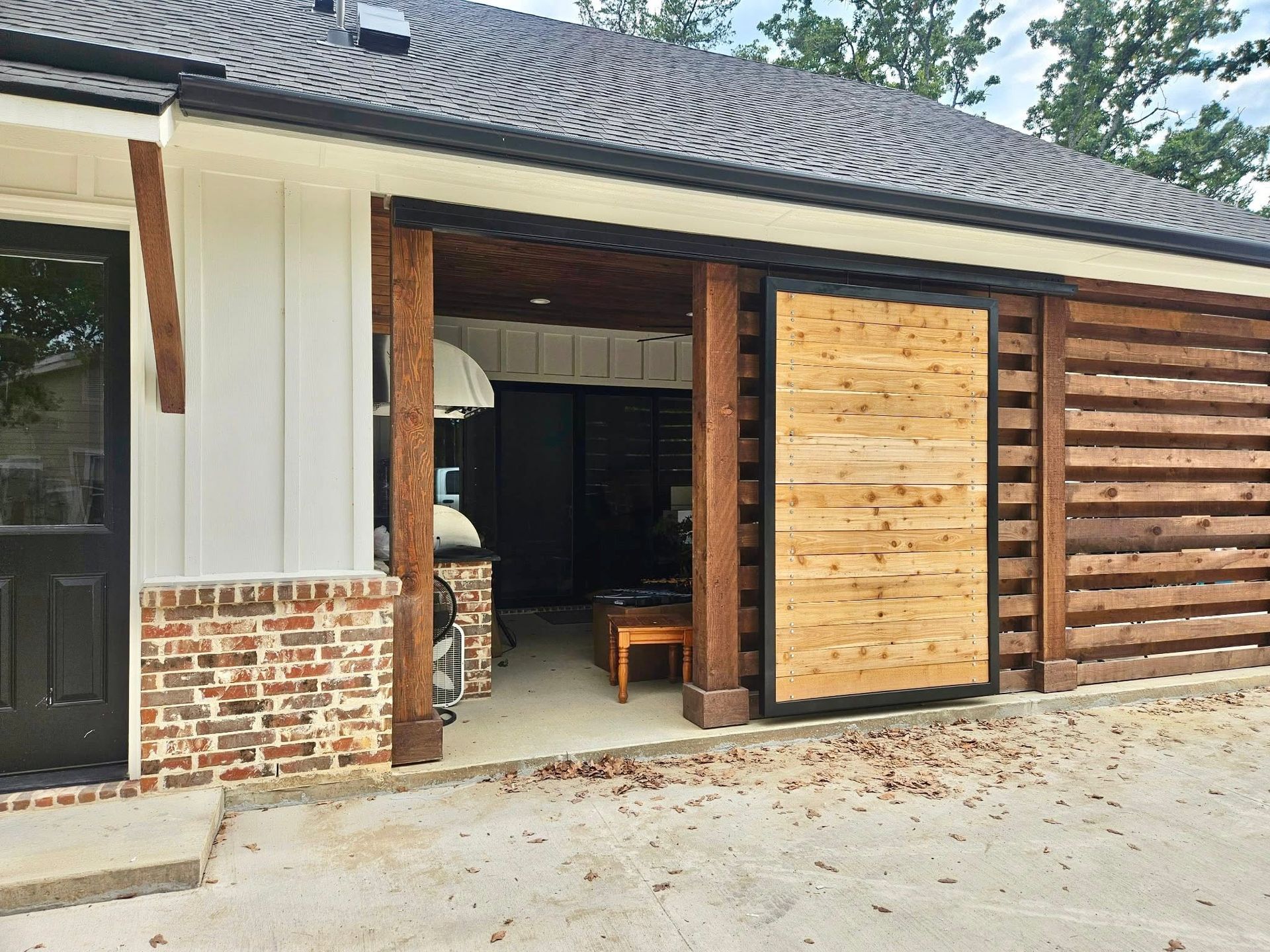Exterior of a house with a partially open barn door and stone-accented siding on a gravel driveway.
