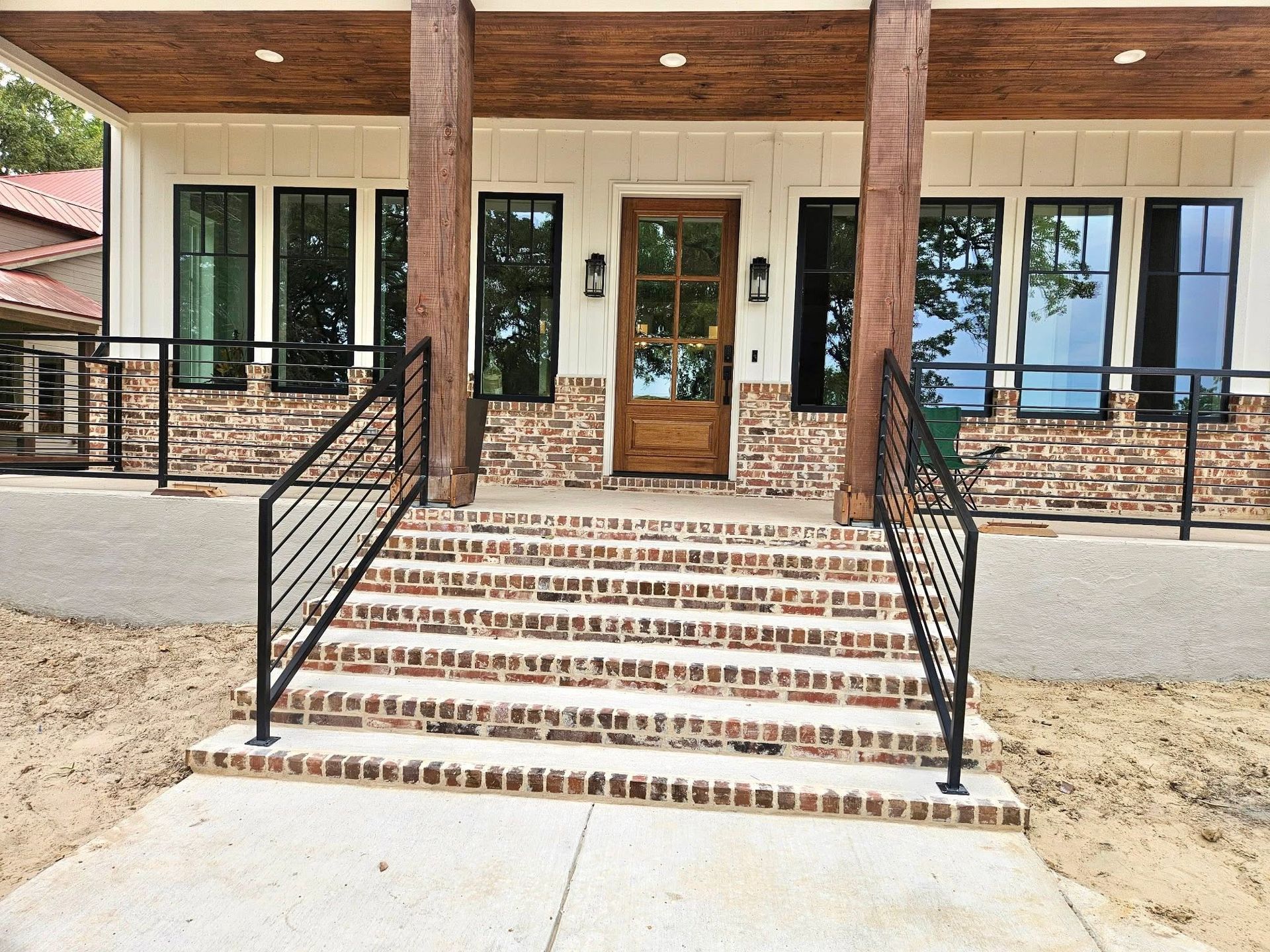 Front entrance of a building with brick steps, black railings, and double glass doors under a covered porch.