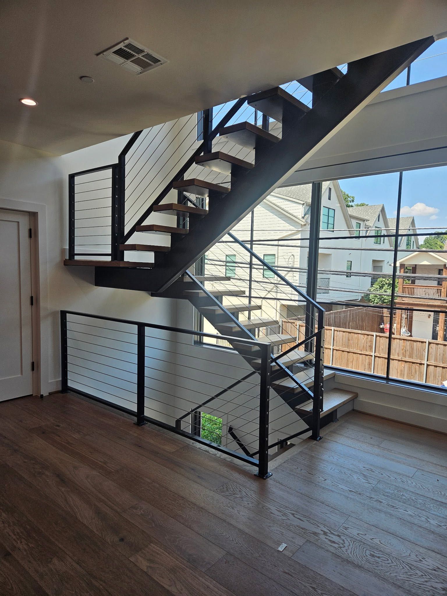 Modern loft interior with black metal staircase, wood floor, and large windows overlooking rooftops.