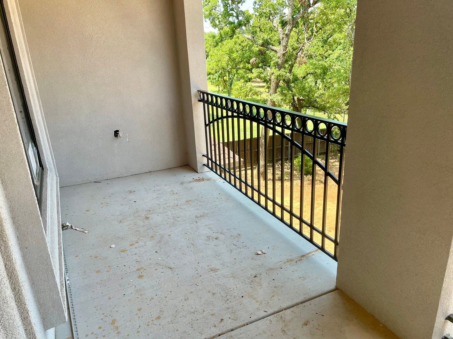 Empty apartment balcony with concrete floor and black metal railing overlooking trees.