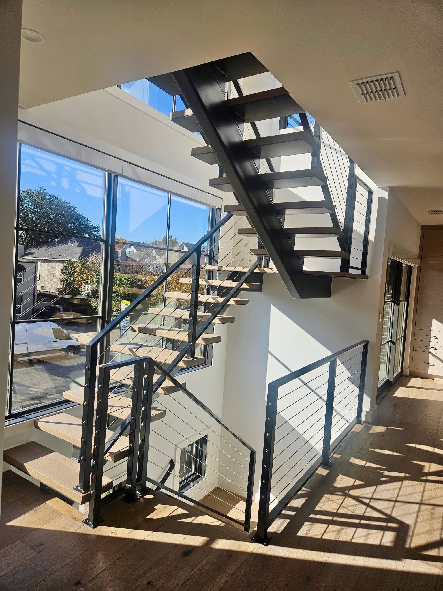 Sunlit indoor stairwell with black metal stairs and railings overlooking a bright courtyard.