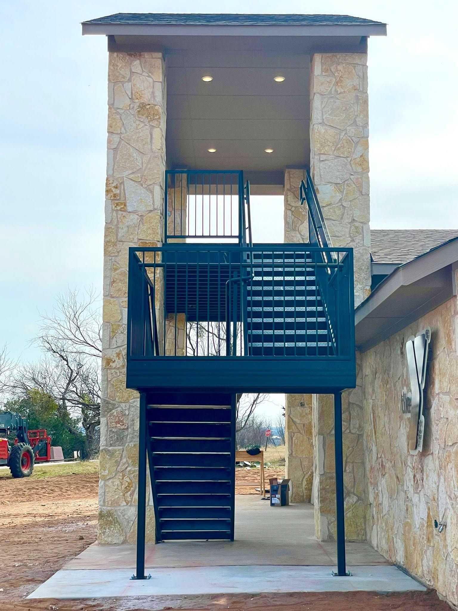 Exterior staircase leading to a raised entrance on a stone building, with a metal landing and stairs above and below.