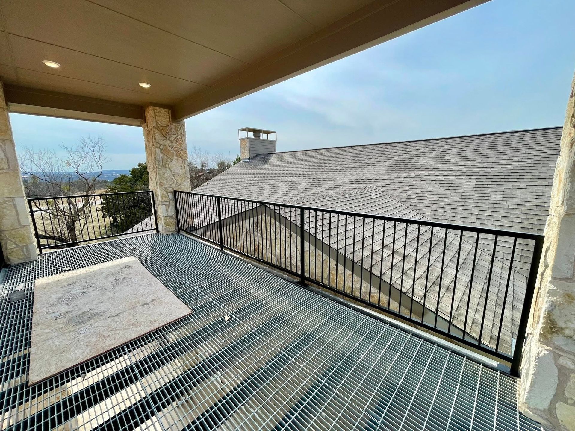 Covered patio deck with black railing overlooking a tiled rooftop and distant landscape.