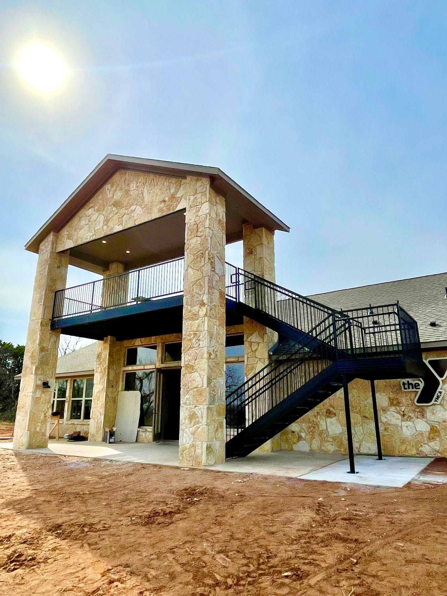 Two-story stone building with black metal stairs under a bright sun in a snowy, muddy yard.