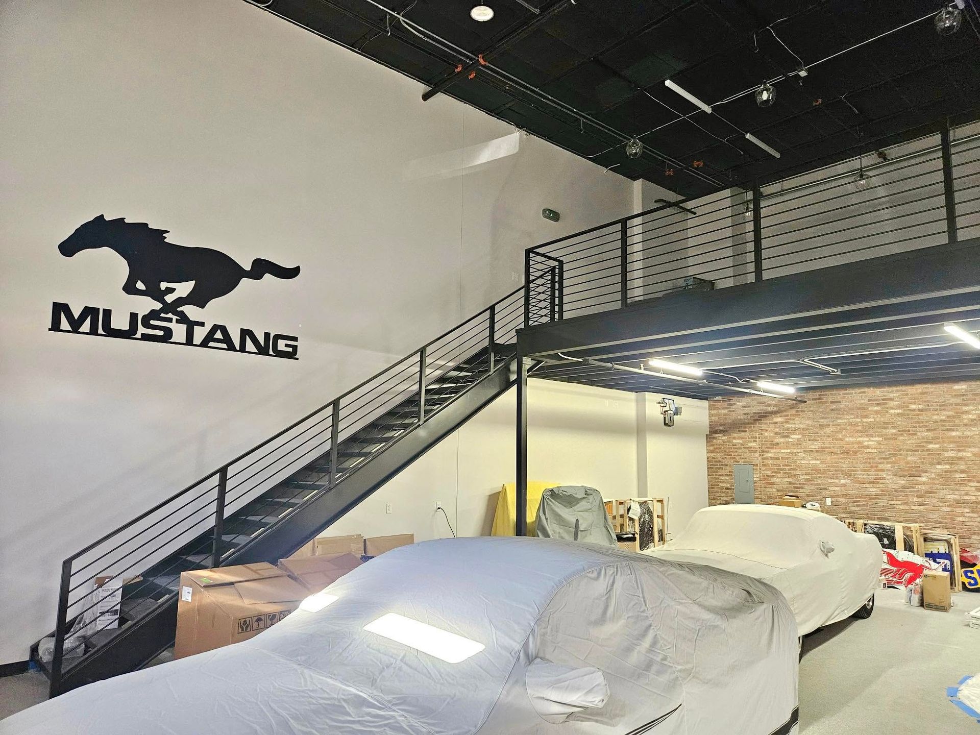 Mustang logo wall above covered cars in an indoor garage with a staircase.