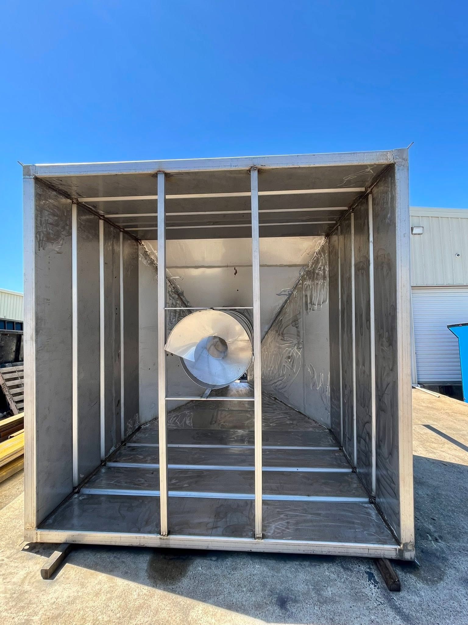 Large square industrial duct or ventilation housing with a circular opening, outdoors under a blue sky.