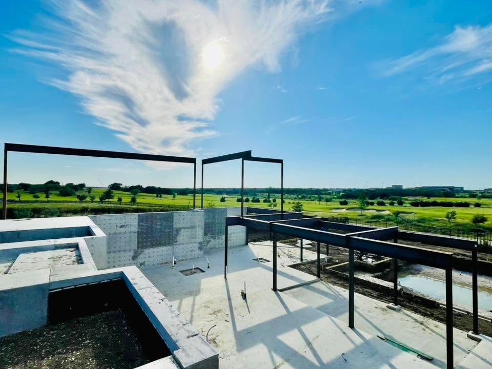 Modern patio with glass railings overlooking a green landscape under a blue sky.