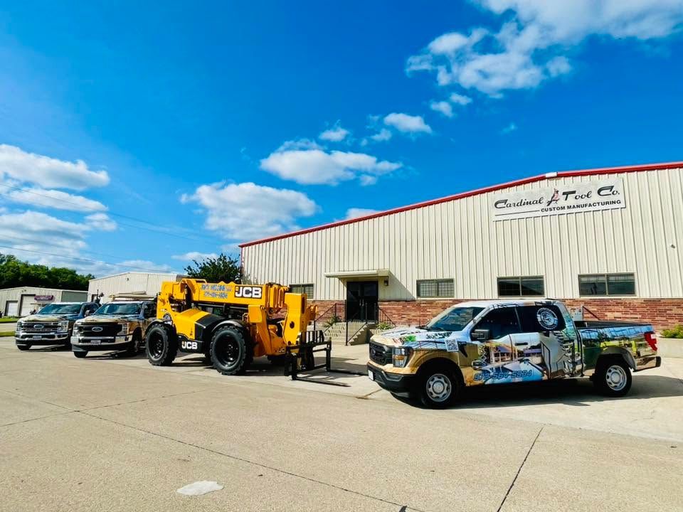 Tow truck and pickup trucks parked outside a beige auto shop under a blue sky.