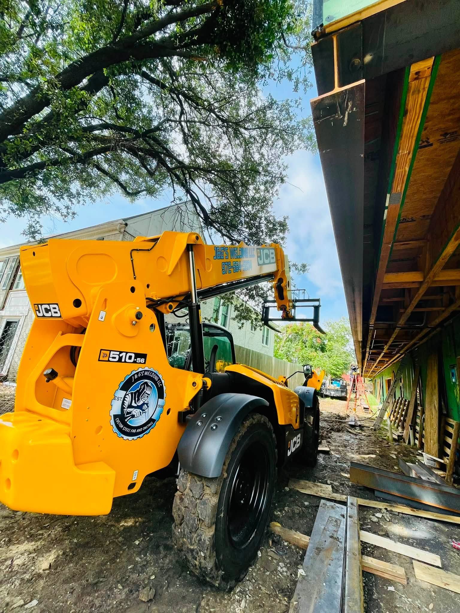 Yellow construction loader beside a building, parked on a muddy roadside under trees.