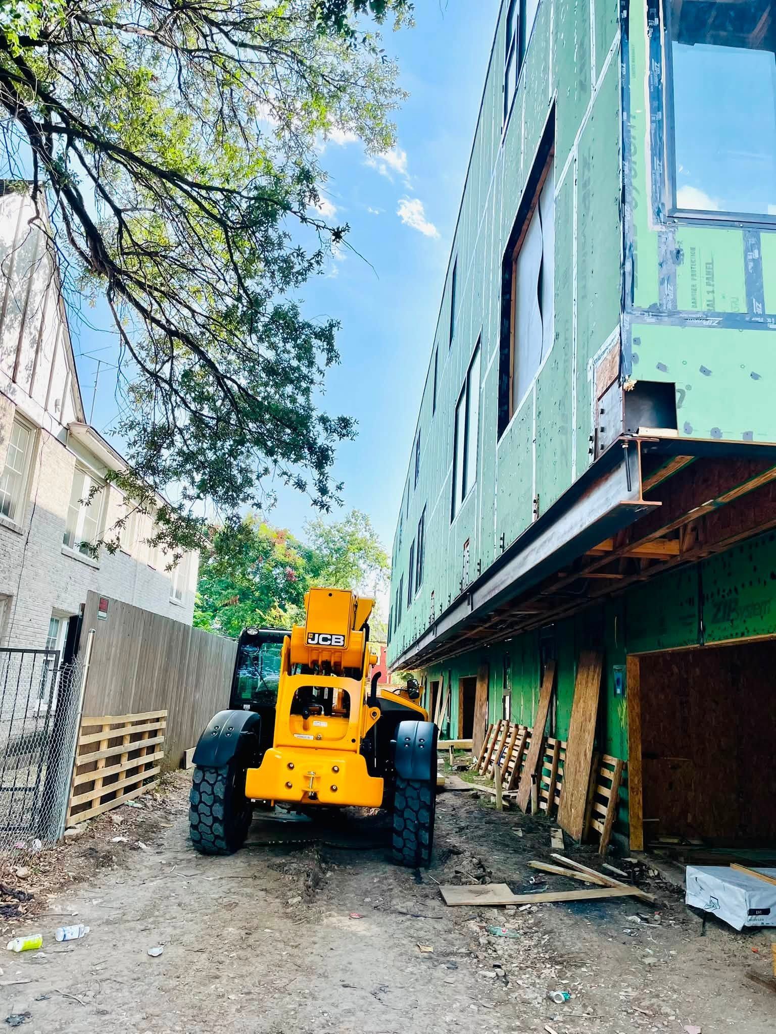 Yellow construction loader in a narrow alley beside a green building under construction.