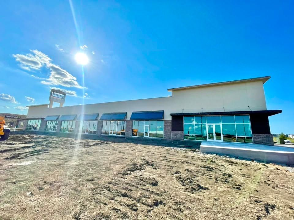 Modern storefront building with large windows and blue sky on a dirt lot.
