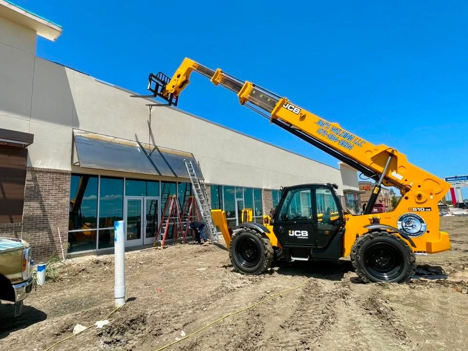 A yellow telehandler is lifting materials beside a building under construction.