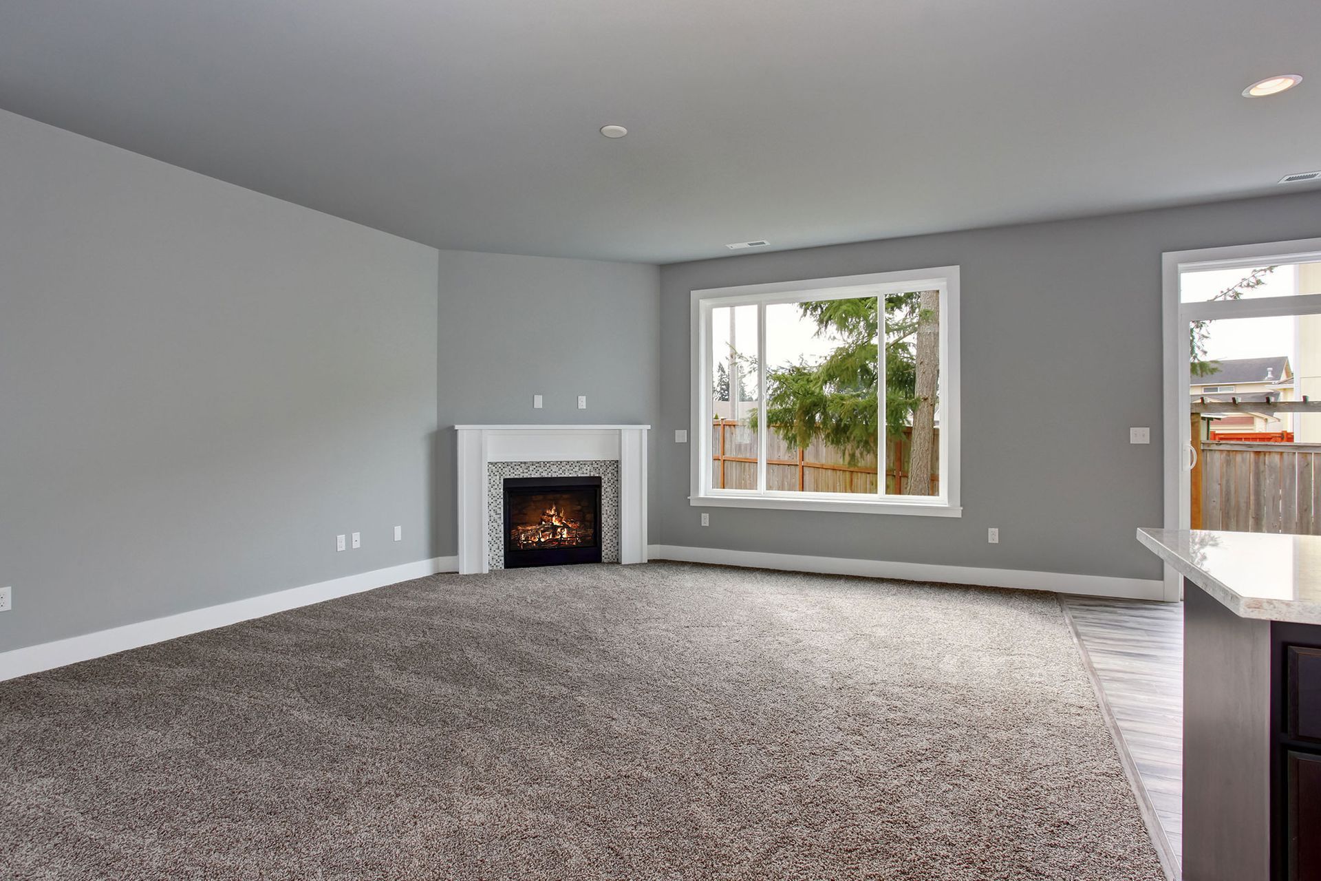 Empty living room with fireplace, window, gray walls, and light gray carpet.