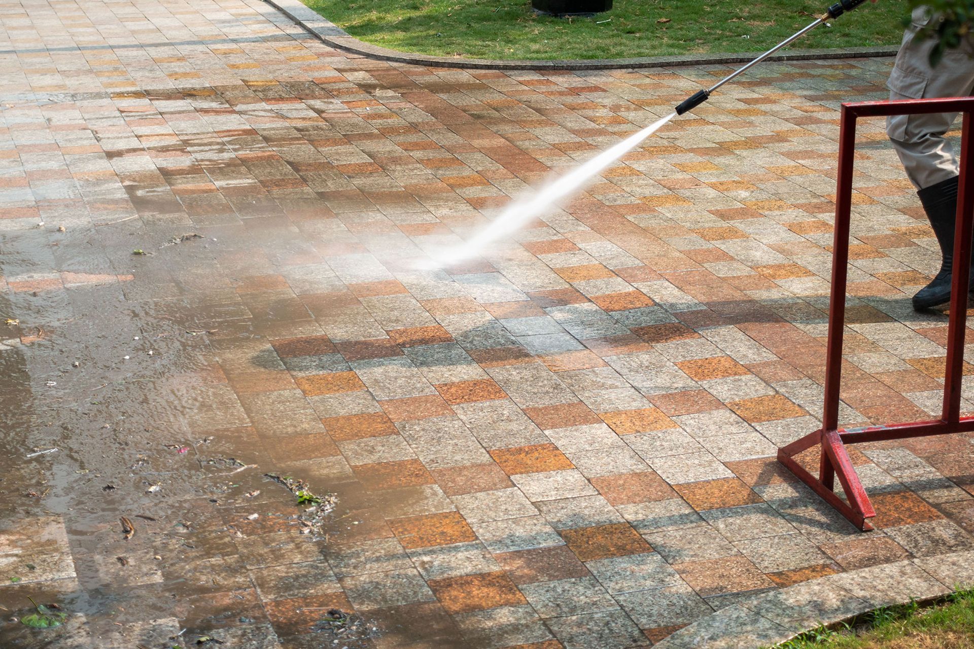 Person power washing a brick walkway outdoors. Water sprays, cleaning the paving stones.
