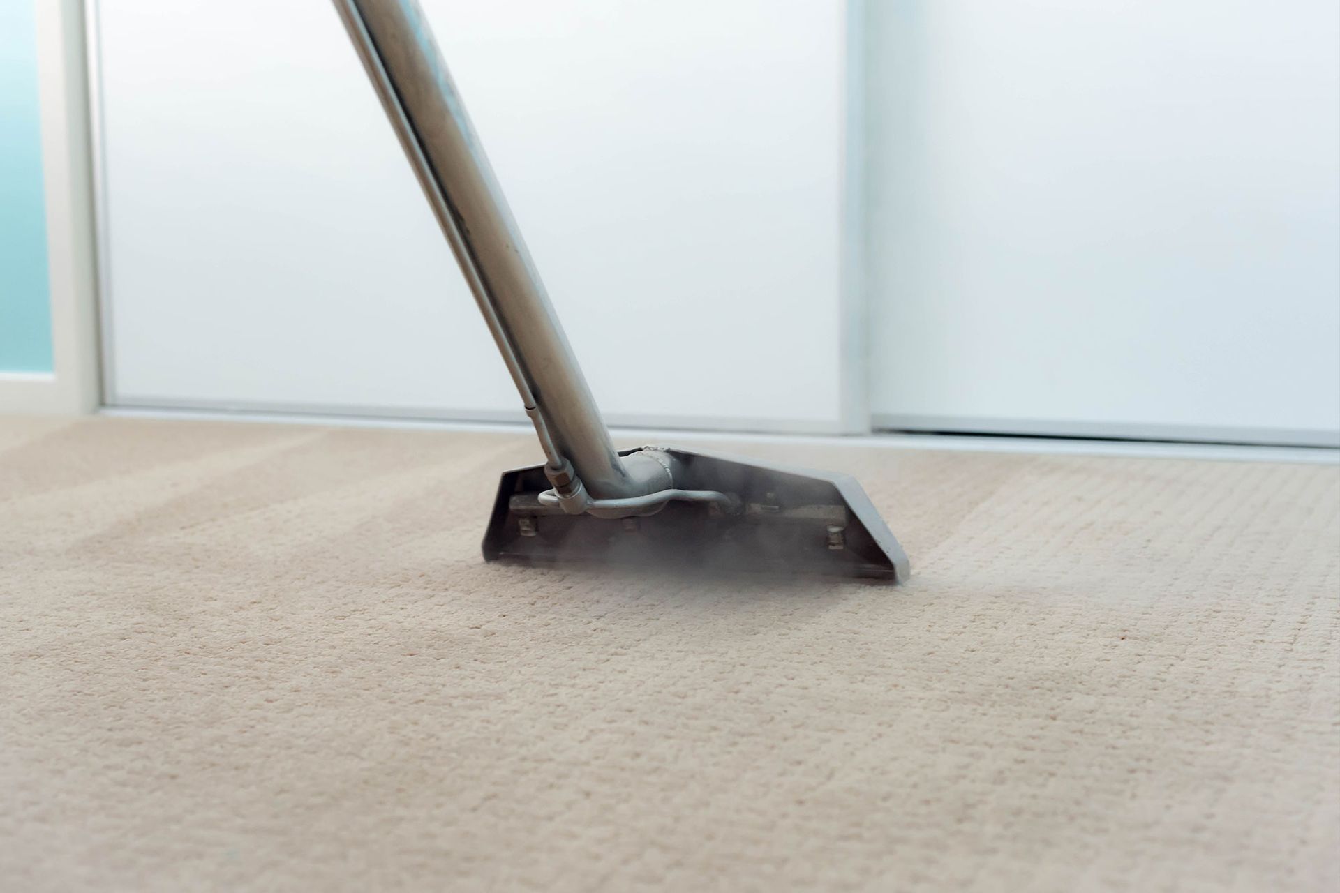 Carpet being cleaned with a steam cleaner, leaving a clean trail in a room.