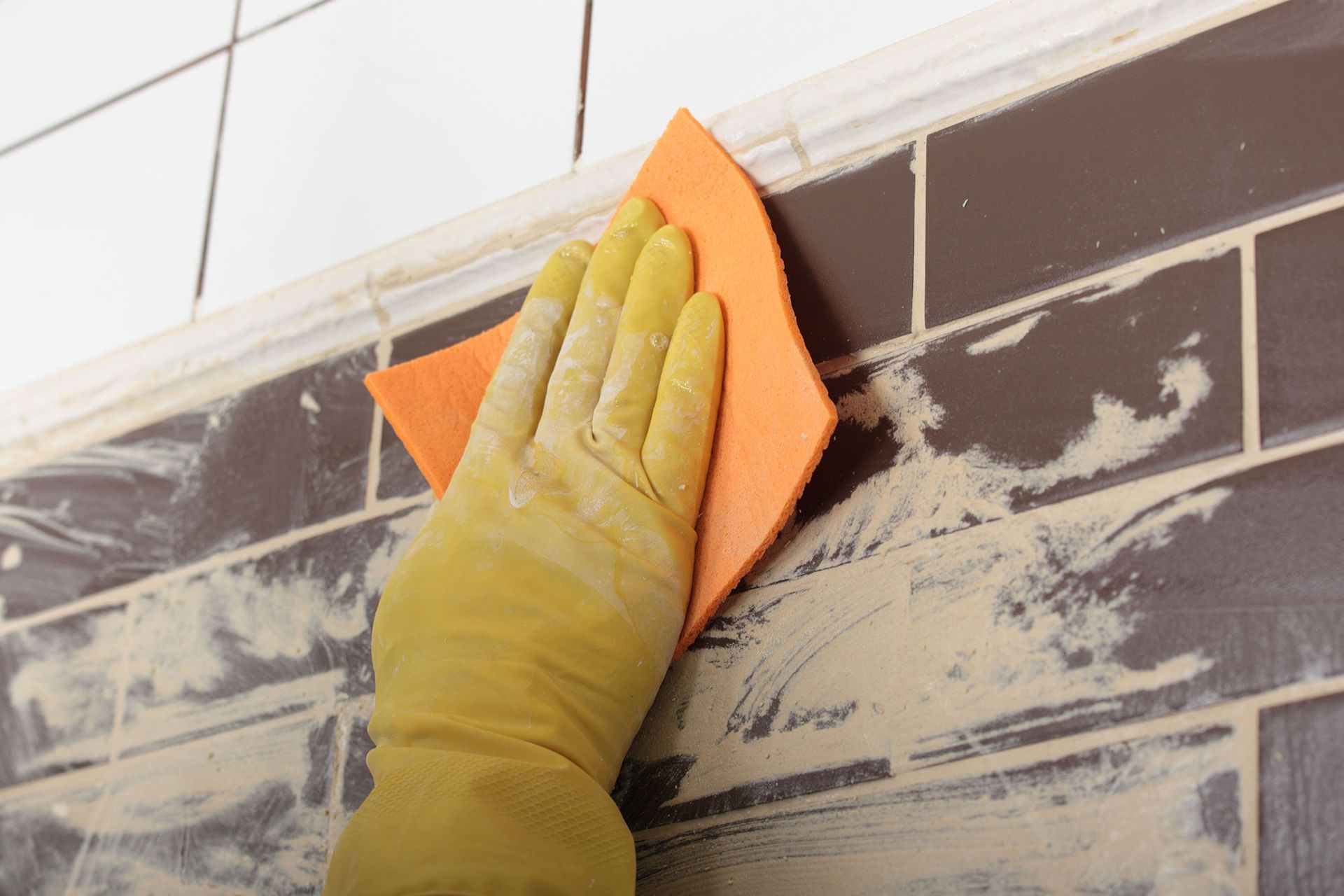 Gloved hand wipes brown tile with an orange cloth; white residue visible.