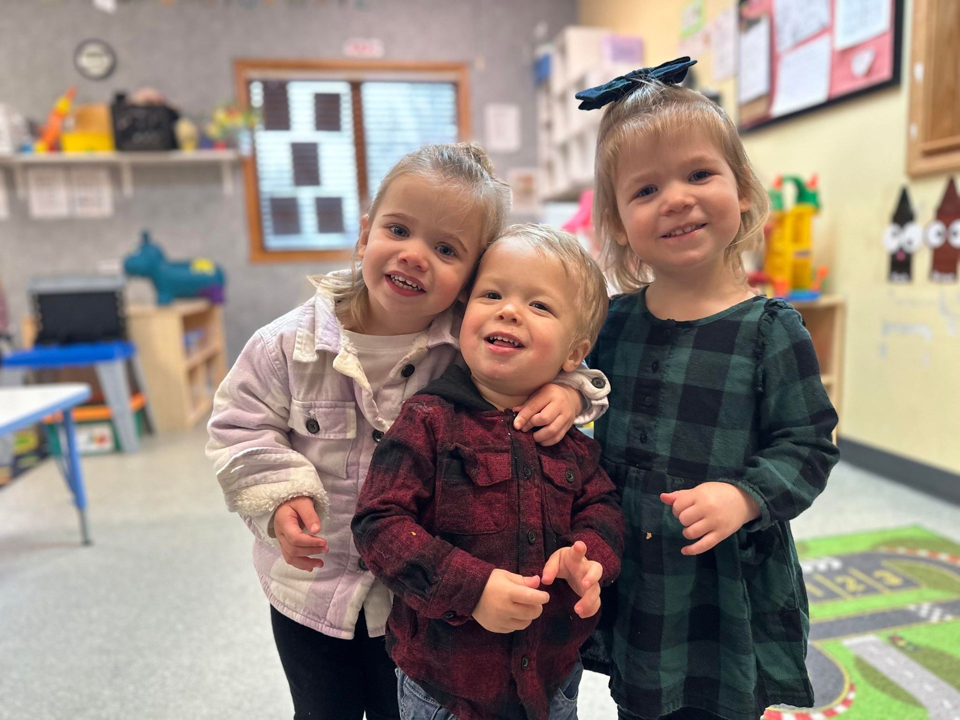 Three young children are posing for a picture in a classroom.