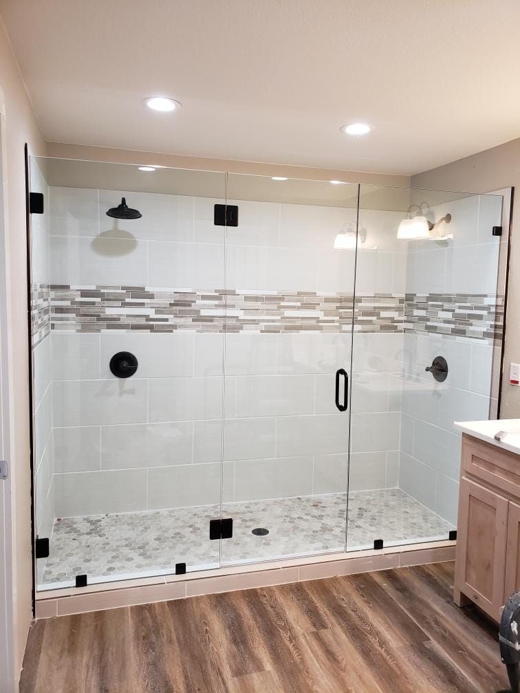 Modern walk-in shower with glass doors, white tile, and wood-look flooring in a bathroom