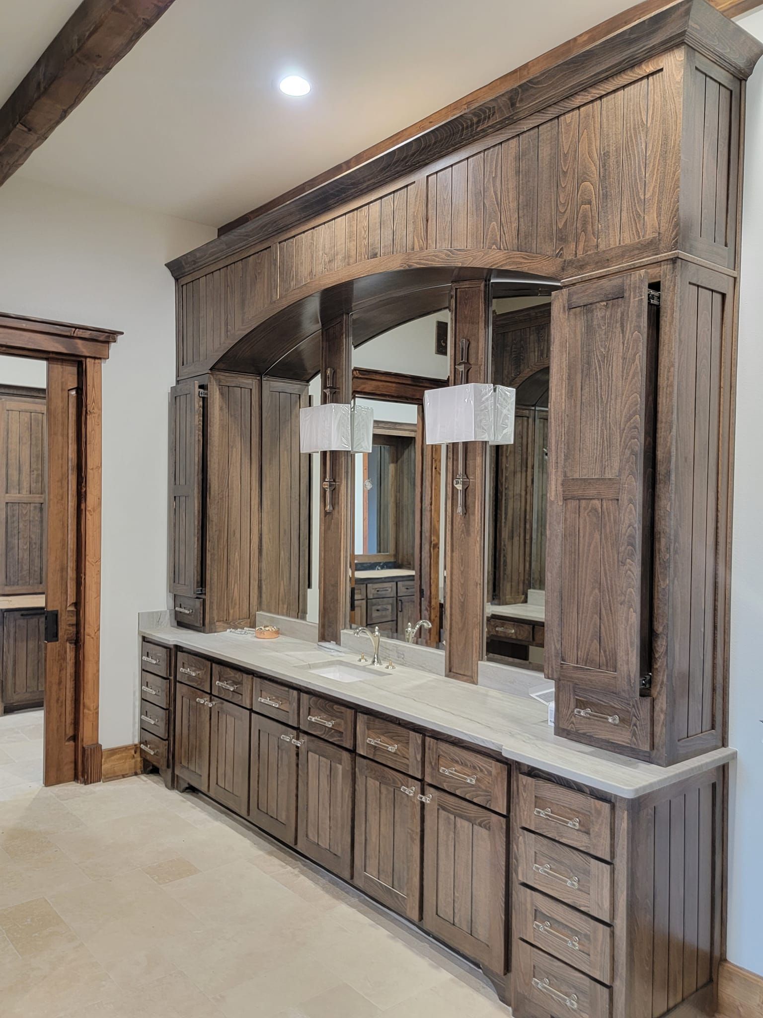Rustic wood bathroom vanity with twin mirrors, cabinets, and cream countertop against beige walls
