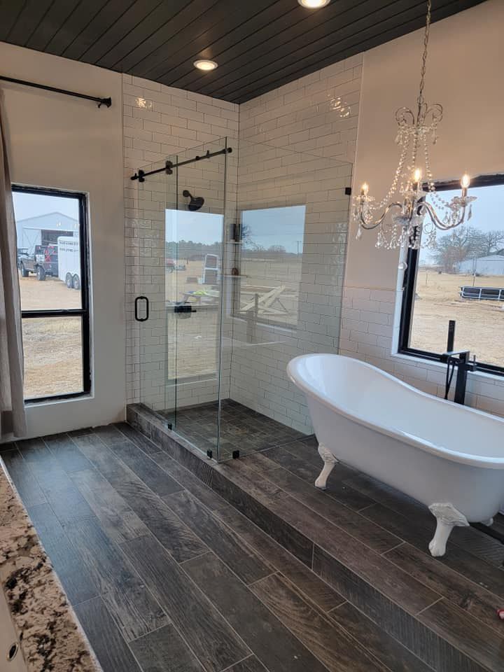 Modern bathroom with glass shower, freestanding white tub, dark wood floor, and chandelier lighting
