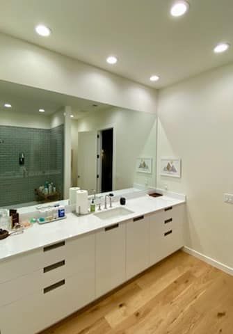 Modern bathroom vanity with white cabinets, double sink, large mirror, and wood floor