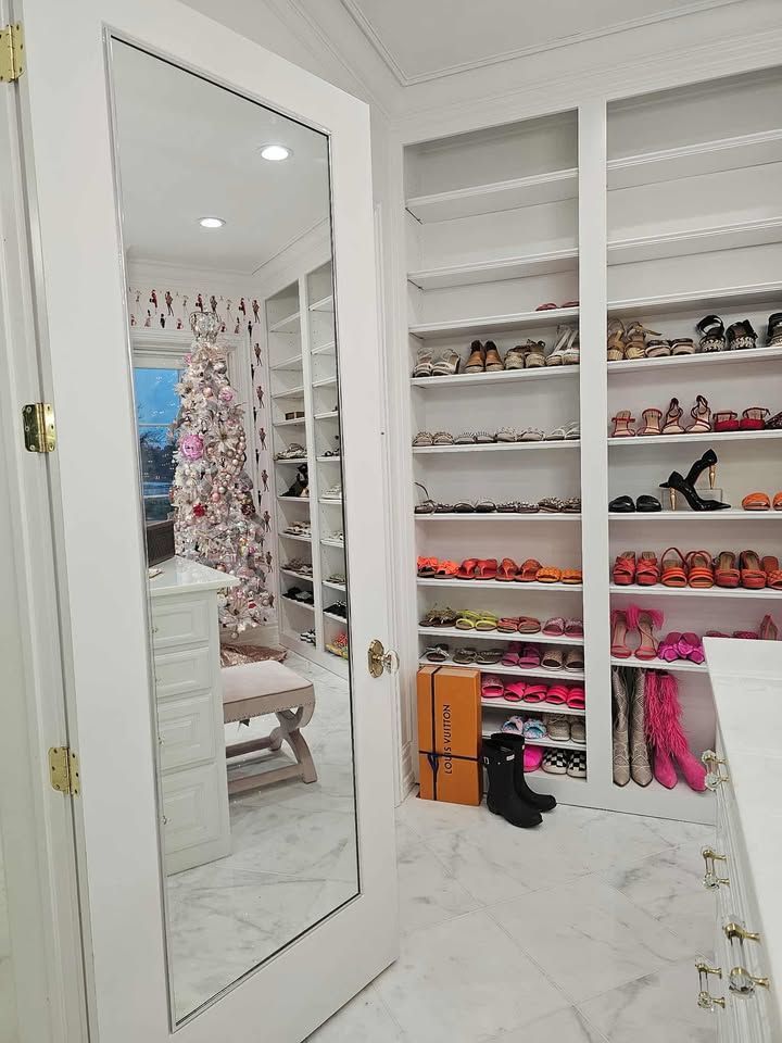 Walk-in closet with white shelves, shoes, boots, and a mirrored door reflecting a decorated room