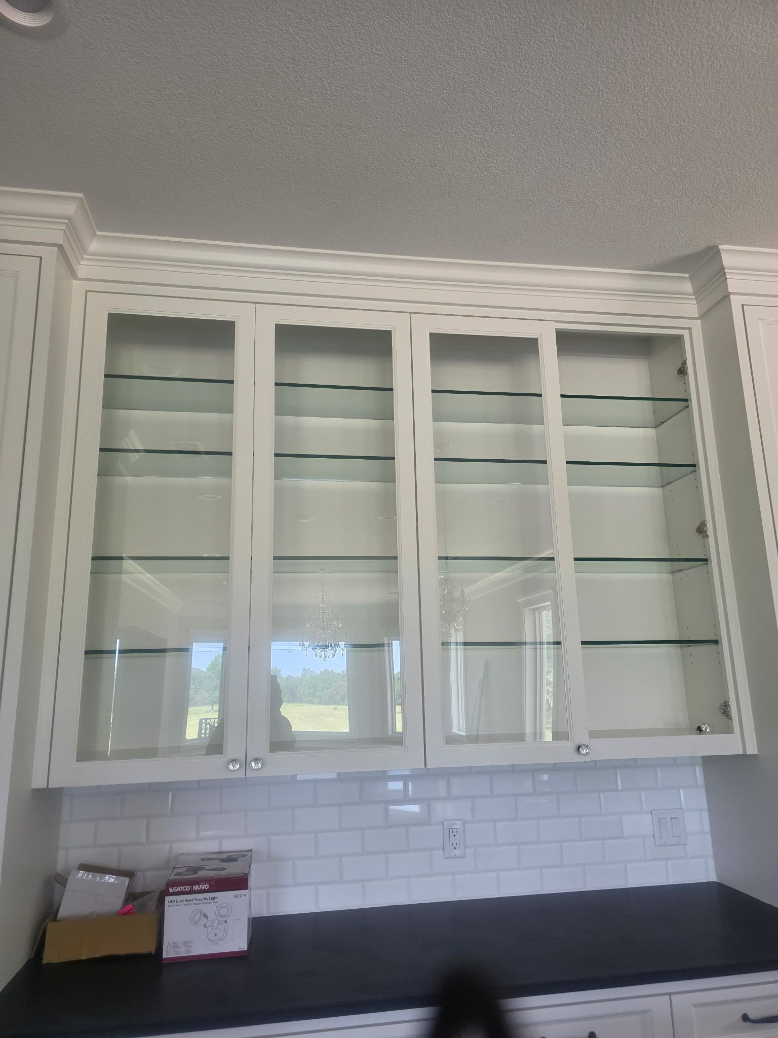 White kitchen cabinets with glass doors above a black countertop and white subway tile backsplash.