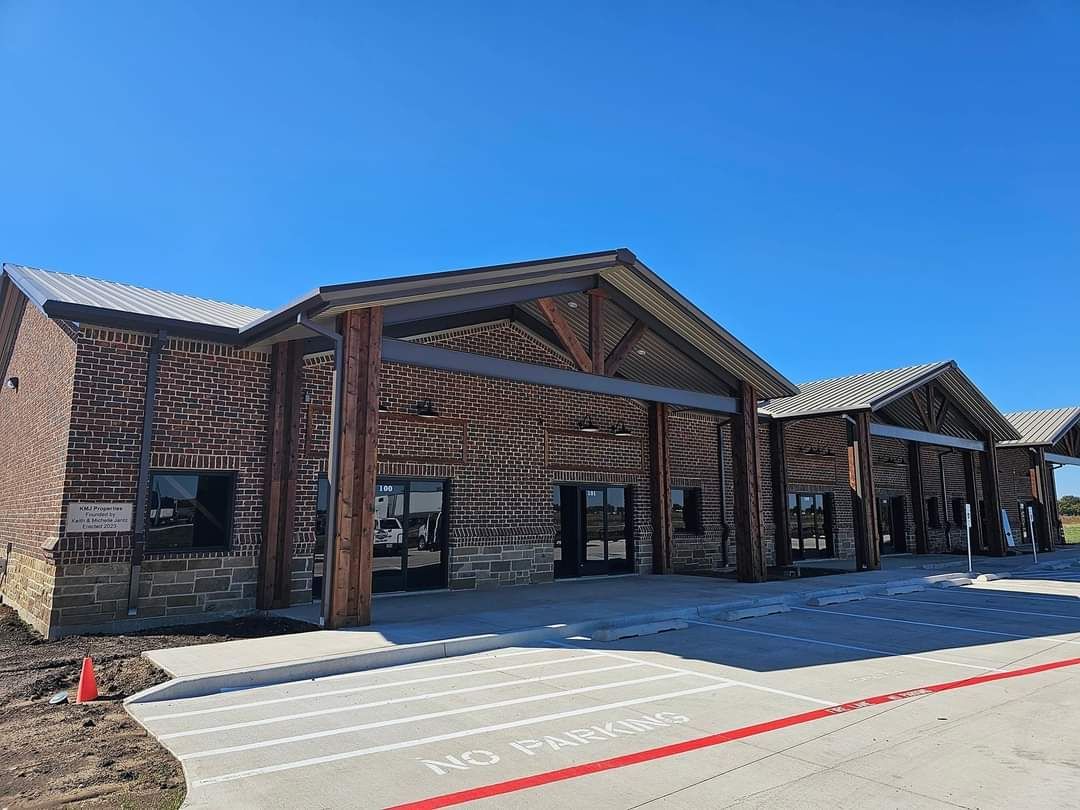 Brick building with timber beams and sloped roofs, front entrance under a bright blue sky.