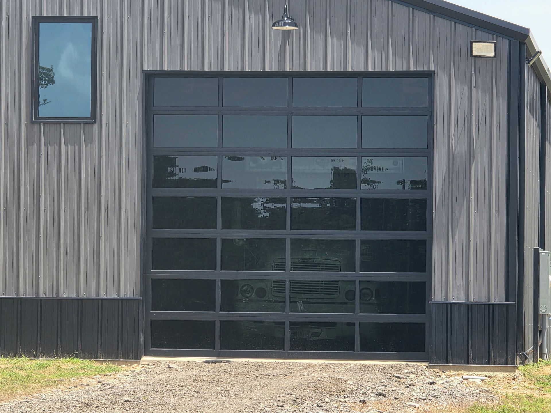 Gray metal building with a large black glass garage door and a small blue window