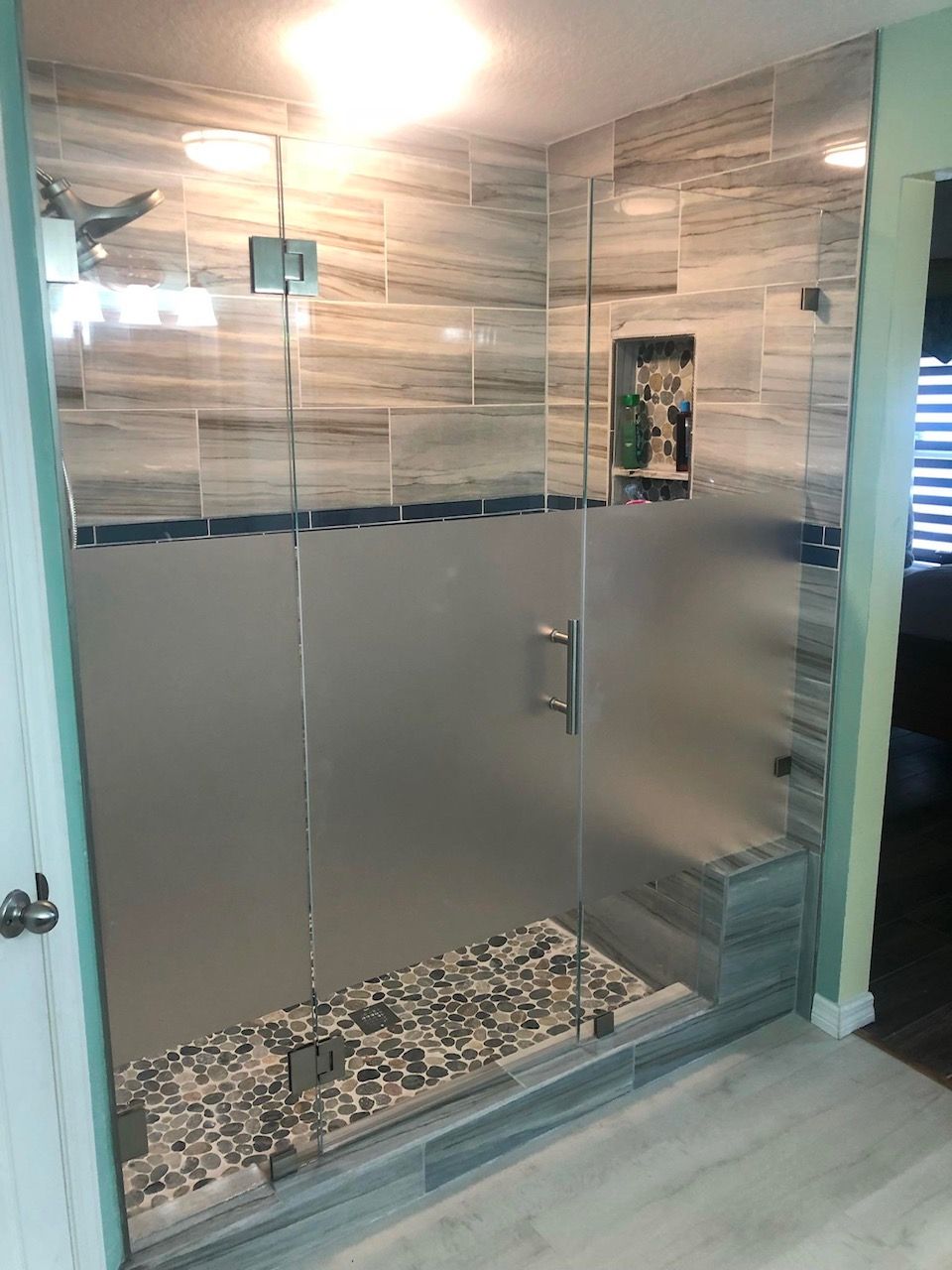 Modern bathroom shower with frosted glass doors and pebble-tile floor accent